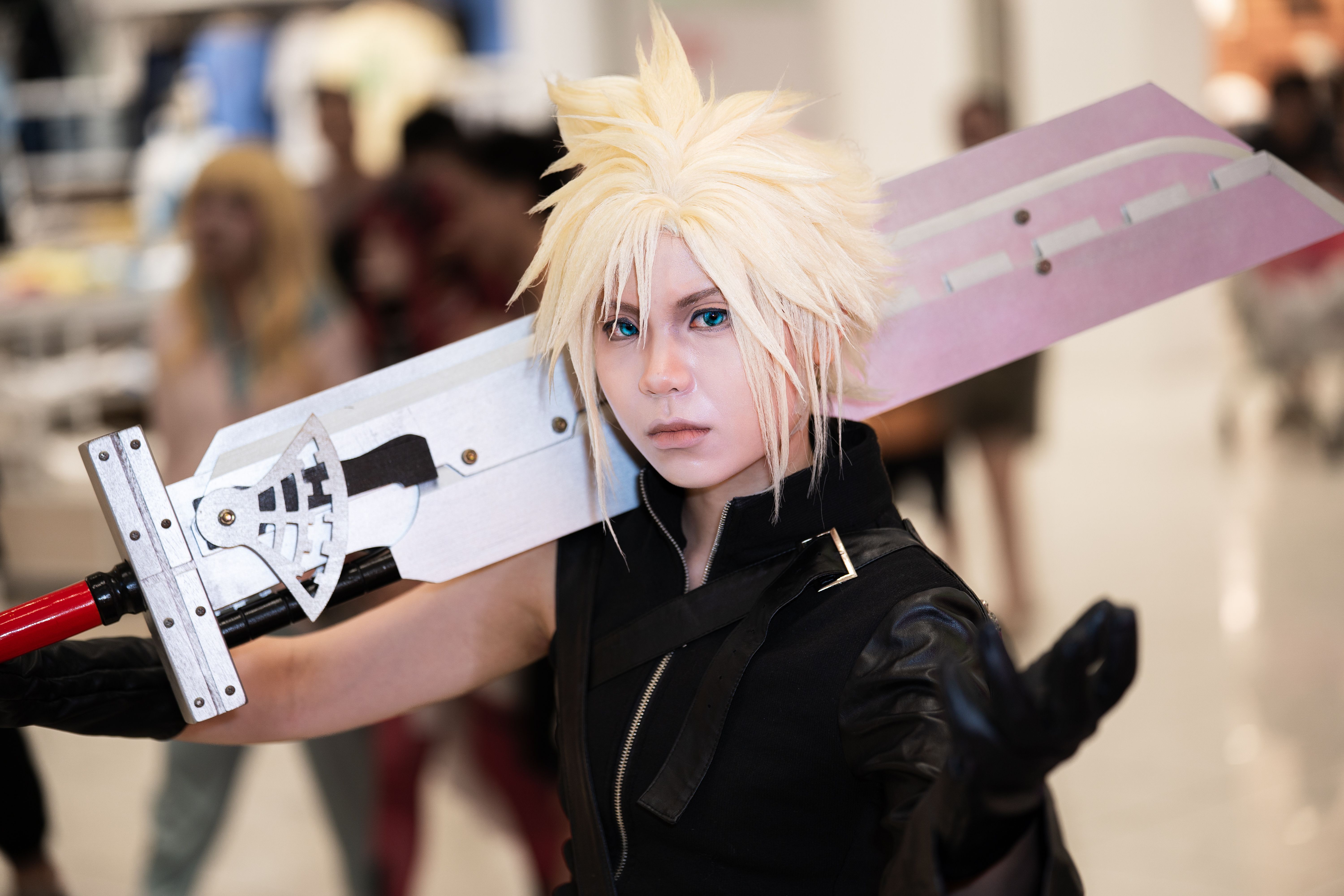 Cosplayer in an elaborate character costume carrying a large sword at a convention.